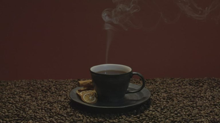 A steaming cup of coffee on a bed of roasted coffee beans