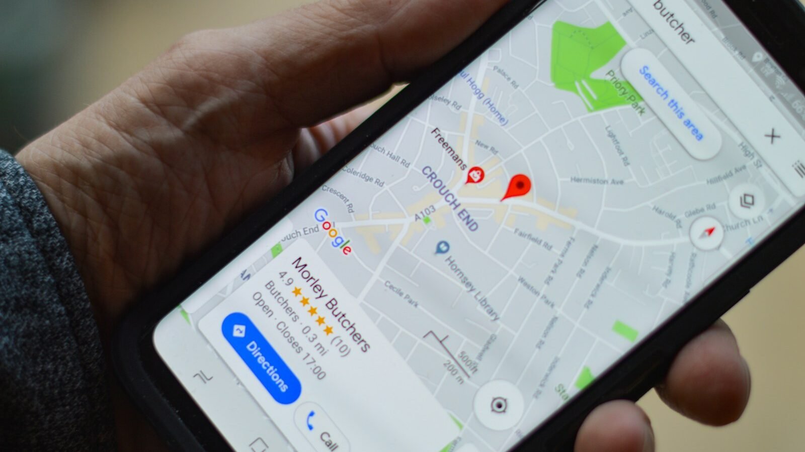 A hand holding a smartphone that shows a map with a local business listing, a star rating and a Directions button.