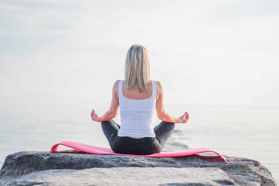 A woman meditating on a flat rock by the sea