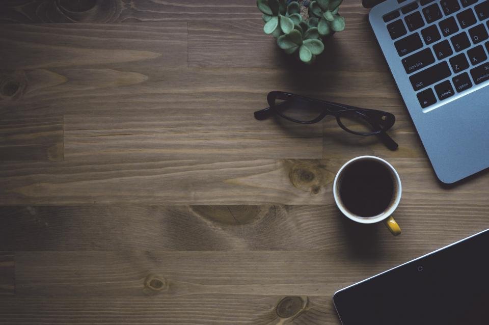 A laptop, glasses and a cup of coffee on a wooden desk